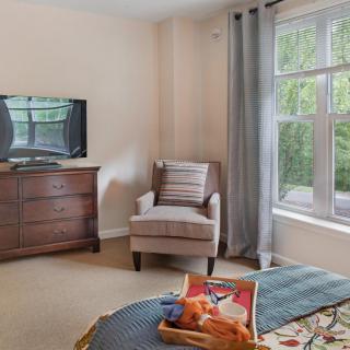 A cozy living room setup with a comfortable chair, a TV on a dresser, and a large window with curtains.