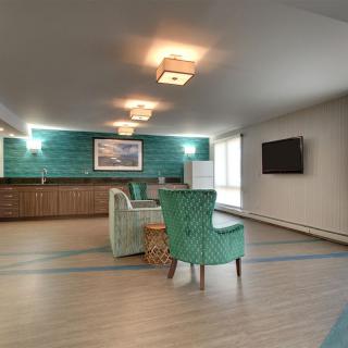 A spacious lounge with modern decor, featuring teal armchairs and a wall-mounted television.