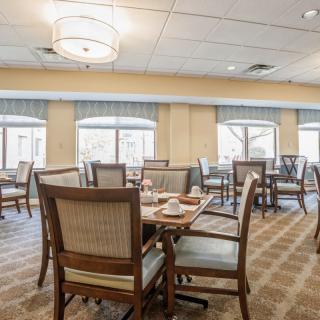 A spacious and elegantly furnished dining area with multiple tables and chairs, featuring large windows and stylish lighting.