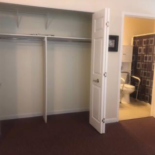 An empty closet with an adjacent bathroom visible through an open door.