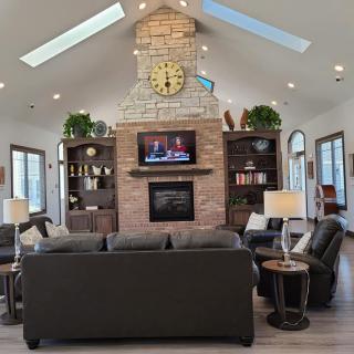 A cozy living room with a central fireplace, surrounded by sofas and bookshelves, featuring skylights and a television above the mantel.