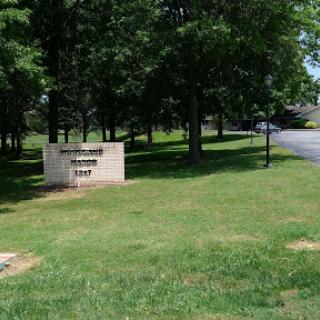 A view of a sign surrounded by trees and grass alongside a road.