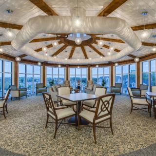 A spacious dining area with elegantly arranged tables and chairs, featuring a unique ceiling design and large windows offering an inviting ambiance.
