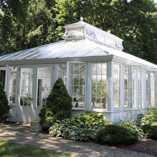 A charming glass greenhouse surrounded by lush greenery in a garden setting.