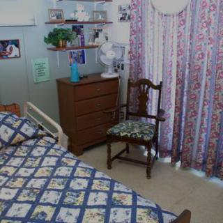 A cozy bedroom with a patterned bedspread, a wooden chair, and decorative curtains.