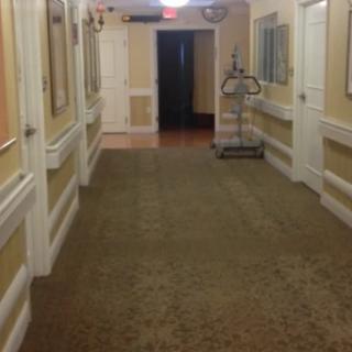 A hotel hallway with a carpeted floor and a luggage cart near the end.