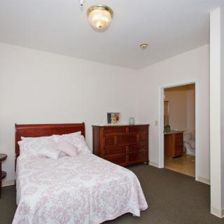 A cozy bedroom featuring a bed with white bedding, a wooden dresser, and an adjoining bathroom.