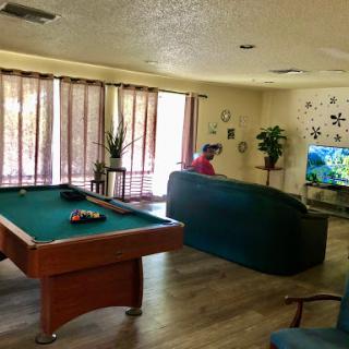 A cozy living room featuring a pool table, comfortable seating, and a television, illuminated by natural light.