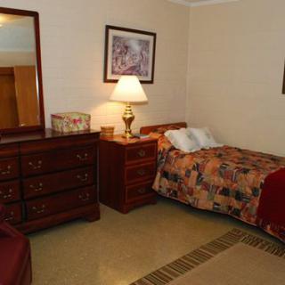 A cozy bedroom with a single bed, dresser, and lamp.