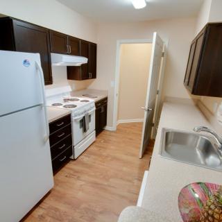 A modern apartment kitchen with dark cabinets, white appliances, and a sleek countertop.