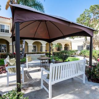 A cozy outdoor gazebo with white benches in a sunny garden setting.