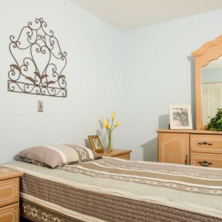 A cozy bedroom with a neatly made bed, wooden furniture, decorative wall art, and fresh flowers.