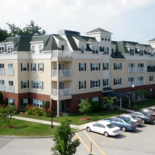 A residential apartment building with a parking lot and landscaped surroundings.