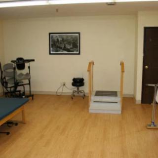 A small gym with various fitness equipment and wooden flooring.