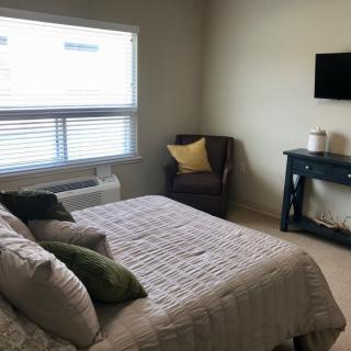 A cozy bedroom featuring a neatly made bed, an armchair with cushions, and a mounted television.