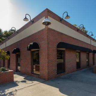 A corner view of a brick building with black awnings and outdoor lighting.