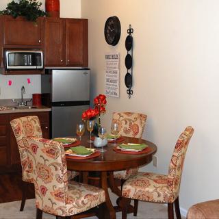 A cozy dining area with a wooden table and floral-patterned chairs next to a compact kitchen.