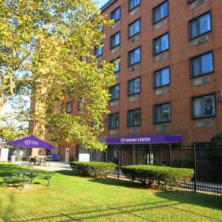 A brick apartment building with purple awnings and a grassy area in front, surrounded by trees on a sunny day.