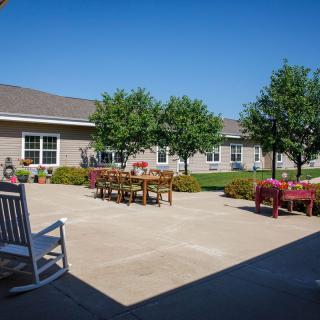 A sunny courtyard with outdoor tables and chairs surrounded by trees and a building.