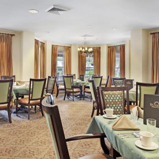 An elegant dining room with neatly arranged tables and chairs, featuring warm lighting and large windows with curtains.
