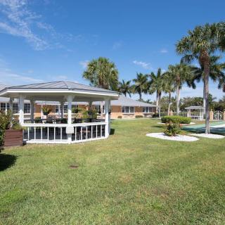 A sunny park scene featuring a gazebo surrounded by palm trees and a well-manicured lawn.