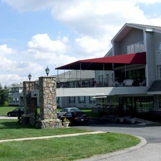 A building with a red awning and stone pillar in the foreground, surrounded by a parking area and grassy landscape.