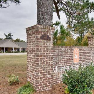 A brick signpost stands at the entrance to a property with a building visible in the background, surrounded by trees and greenery under an overcast sky.
