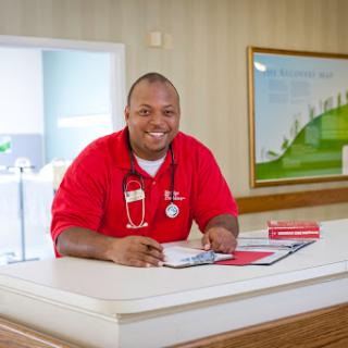 A friendly healthcare worker in a red uniform smiles at the reception desk.