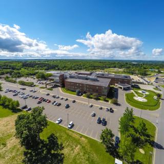 A beautiful aerial view of a modern building surrounded by a spacious parking lot and lush greenery under a clear blue sky.