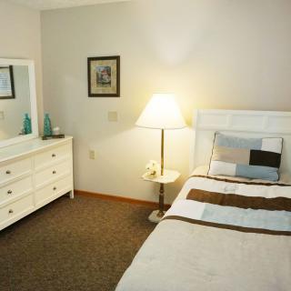 A cozy bedroom with a single bed, dresser, and floor lamp.