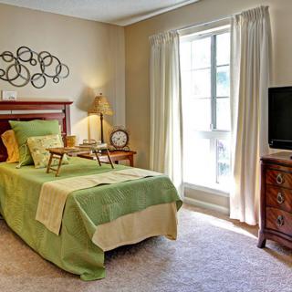A cozy bedroom with a green-themed bedspread, wooden furniture, and natural light from a large window.