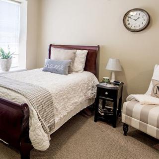 A cozy bedroom with a single bed, nightstand, and chair, featuring neutral tones and minimal decor.