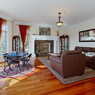 A spacious living room with a fireplace, brown sofas, and a small dining area on wooden flooring.