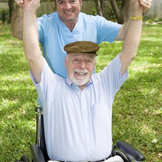 Happy elderly man in a wheelchair with caregiver outdoors.
