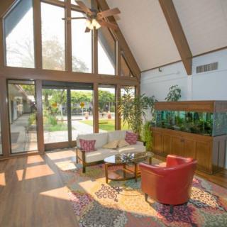 A spacious living room with large windows, high ceilings, and modern furniture, featuring an aquarium and indoor plants.