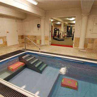 An indoor fitness facility featuring a small swimming pool and a gym area in the background.