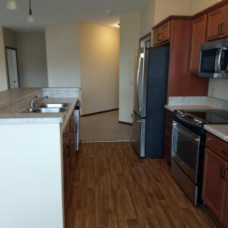 A modern kitchen in an apartment featuring stainless steel appliances and wooden flooring.