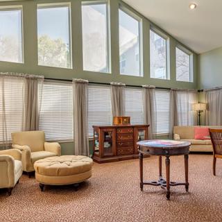 A spacious living room with large windows, featuring modern neutral-colored furniture and abundant natural light.