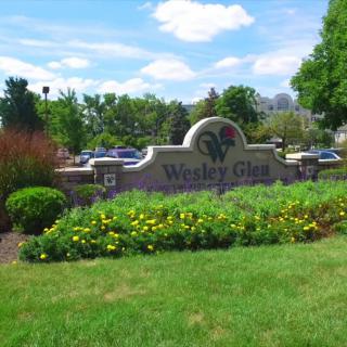A landscaped entrance sign for Wesley Glen surrounded by flowers and trees.