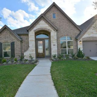 A brick house with a well-maintained front yard and driveway under a partly cloudy sky.