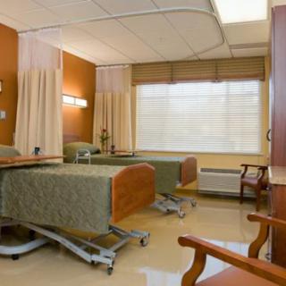 A hospital room with two beds, chairs, and privacy curtains.