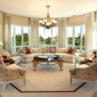 A spacious and elegantly designed living room with a large sectional sofa, a central coffee table, and ample natural light from surrounding windows.