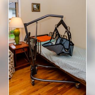 A patient hoist positioned next to a hospital bed in a room.