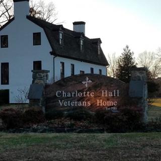 The entrance sign of the Charlotte Hall Veterans Home, set against a backdrop of a historical building.