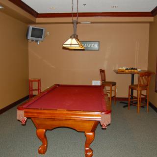 A cozy game room featuring a pool table, wall-mounted television, and bar seating.