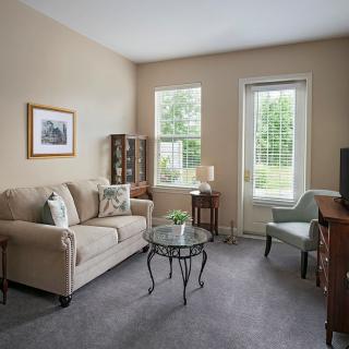 A cozy living room with a sofa, armchair, and a glass coffee table, decorated in neutral tones.