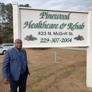 A man stands beside the Pinewood Healthcare & Rehab sign.