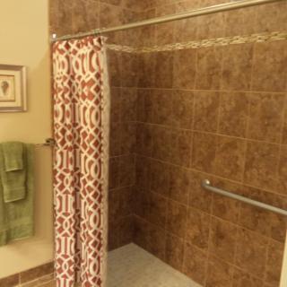 A cozy bathroom featuring a tiled shower with a patterned curtain and safety grab bar.