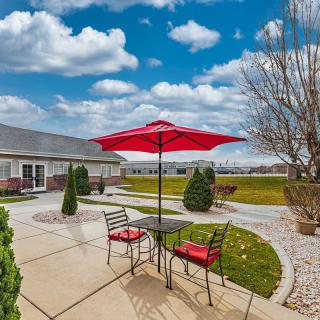 A cozy patio with a red umbrella and chairs under a bright, cloudy sky.