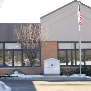 A view of a modern building with an American flag flying in front, surrounded by snow.